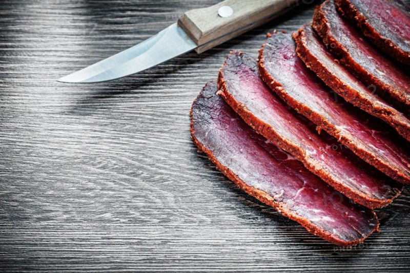 Smoked meat cut into slices, knife on wooden board