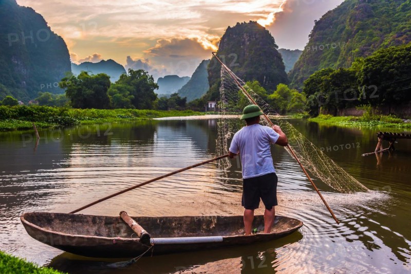 Fisherman on boat in Trang An, a scenic area near Ninh Binh, Vietnam inscribed as a UNESCO World Heritage Site in 2014