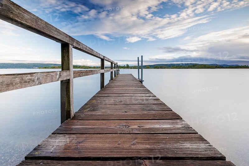 Long wooden footbridge leads into a quiet lake under a partly cloudy sky, Naturfreundehaus, Markelfingen, Untersee, Lake Constance, Kreis Konstanz, Baden-Württemberg, Germany, Europe