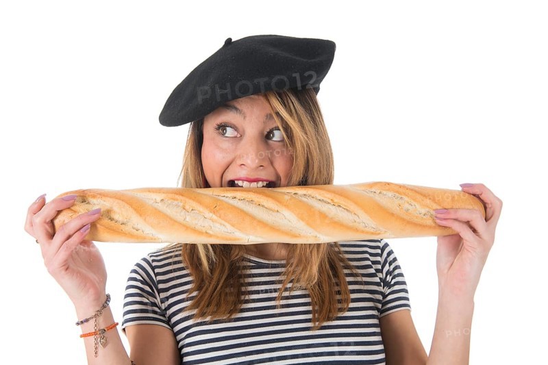 Young French girl with typical French barret and striped shirt eating bread isolated over white background