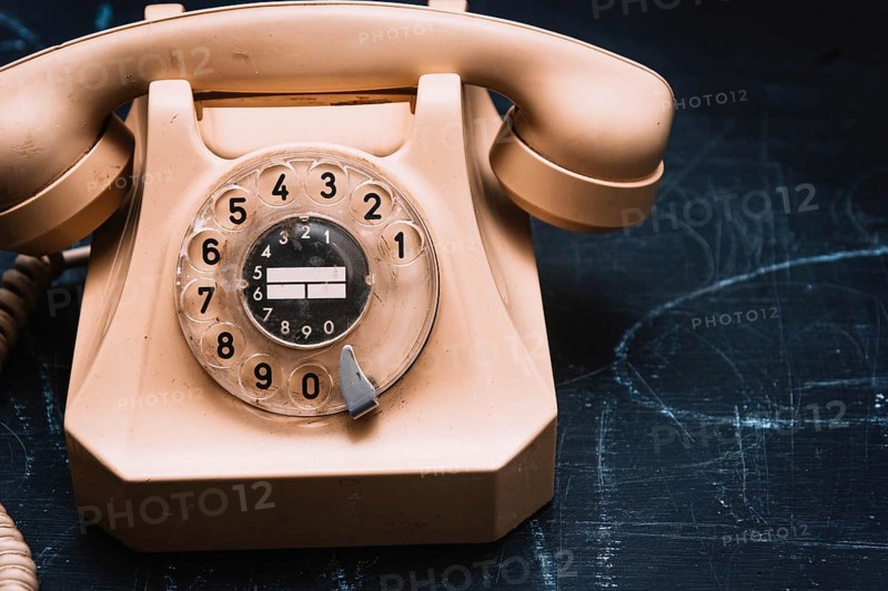 Close-up of a beige vintage rotary phone on a dark surface, evoking a sense of nostalgia