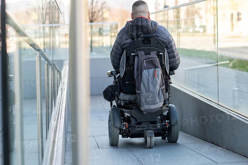 Man in a wheelchair using a ramp next to stairs