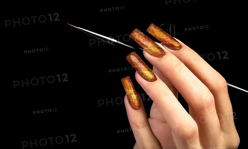 Hand with a beautiful golden manicure and a brush on a black background. Nail design. Extended nails