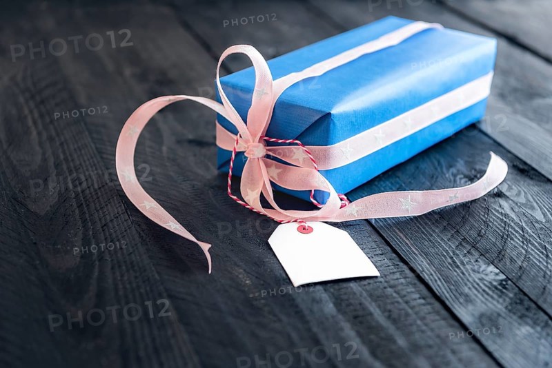 Classy blue gift, tied with pink ribbon and bow, with an empty label tied to it, on an old wooden table