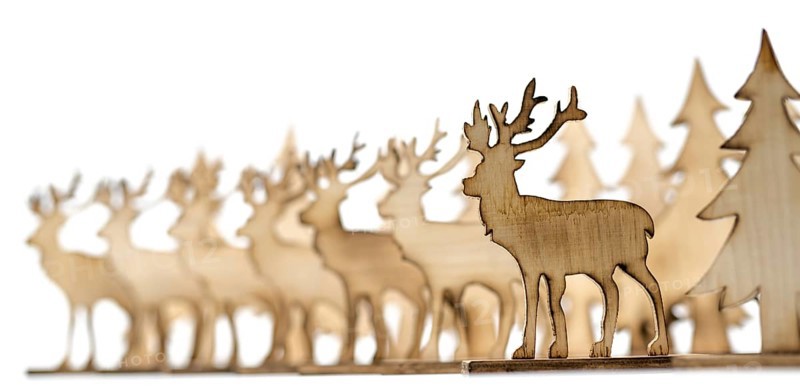 Deer figure sawn out of wood with dark edges and wooden fir trees cut out on white