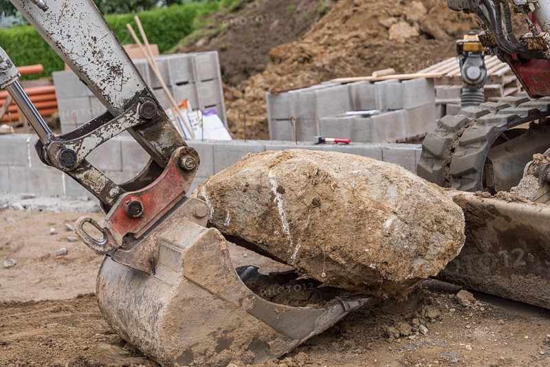 Excavator shovels large stone onto shovel - Construction industry, Construction site