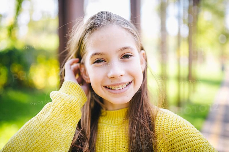 Beautiful and happy teenage girl with braces smiling to camera in yellow clothes in park. Concept of dentist and orthodontist. Pretty teenage girl wearing teeth appliance smiling cheerfully outdoors