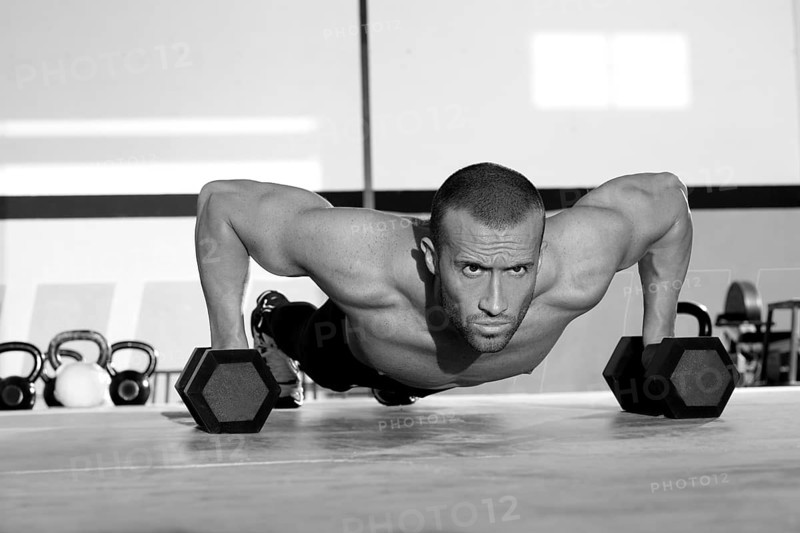 Gym man push-up strength pushup exercise with dumbbell in a crossfit workout