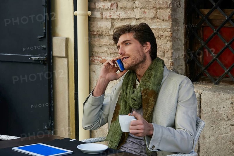 Young man talking smartphone phone in an cafe outdoor sitting having some coffe