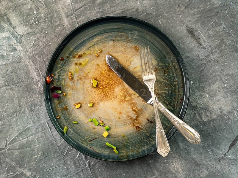 Dirty dish and silverware cutlery on gray background, top view or flat lay. Empty dirty craft plate with fork and knife on gray textured background