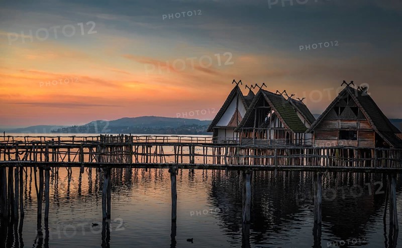 Weathered wooden cabins built on wooden pillars over the Bodensee lake water, at colorful sunset, in Unteruhldingen, Germany, Europe