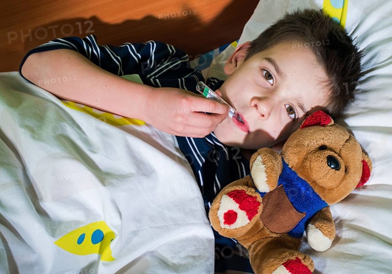 Sick child in bed with teddy bear. Measuring the temperature with a thermometer