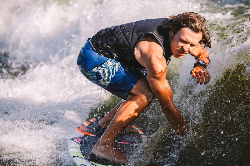 Young athletic man with long hair wakesurfing on waves of river in sunny summer weather. Ttheme outdoor activities in summer. Water sports wakesurf on the board. sliding wakeboarder in water splash