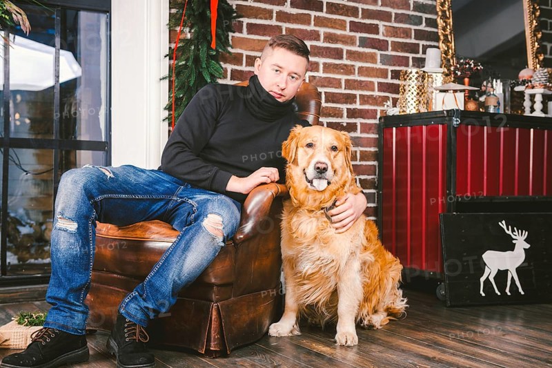 The theme is the friendship of man and animal. Caucasian young male and pet dog breed Labrador Golden Retriever at home inside in winter. Christmas time, New Year holidays