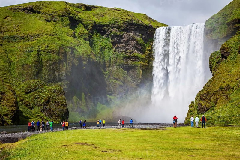 Magnificent famous waterfall Skógafoss, Iceland. A powerful jet Skógar river falls from a large glacier. Tourists delighted the crowd at the foot of roaring jets