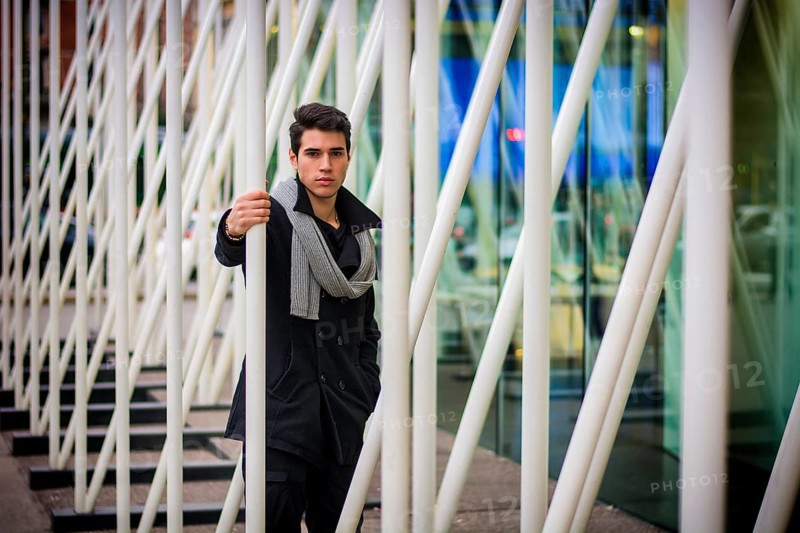 Stylish Young Handsome Man in Black Coat Standing in City Centre Street among White Metal Bars of Moden Architecture