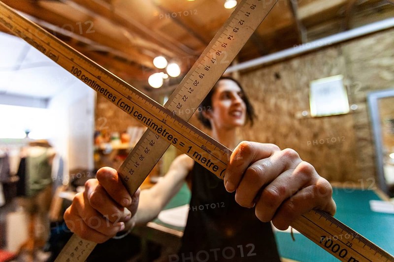 A closeup view of two wood measuring rods being held by a woman tailor inside her retro studio. Artist shows tools used in design process