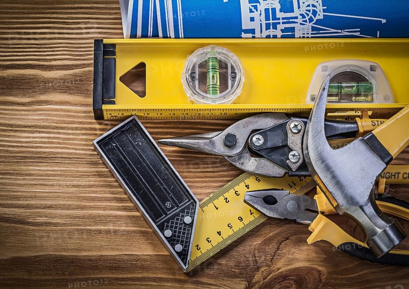Blue blueprints construction level try square claw hammer pliers tin snips on wooden board
