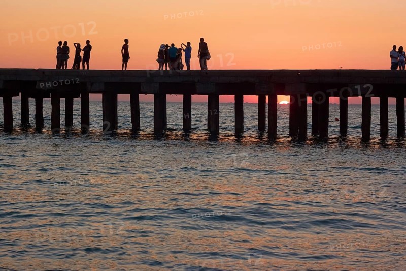 Groups of people on the old pier are photographed and admire the beautiful sunset over the Black Sea coast in Crimea, Ukraine, Europe