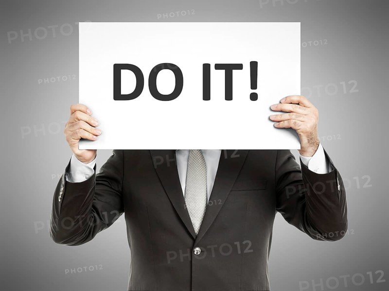 A business man holding a paper in front of his face with the text do it