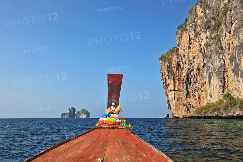 The Thai excursion boat floats to ocean island. The boat nose is decorated by multi-colored and bright silk scarfs