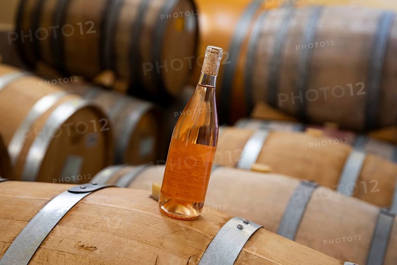 A bottle of rose wine on Oak Barrels wine fermenters in a winery