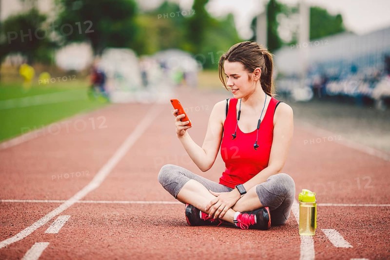 Beautiful fitneß girl uses smartphone at stadium after workout. Sports and healthy. Sport woman use of cellphone inside sport complex. Sport and technology. resting after workout, run at red track