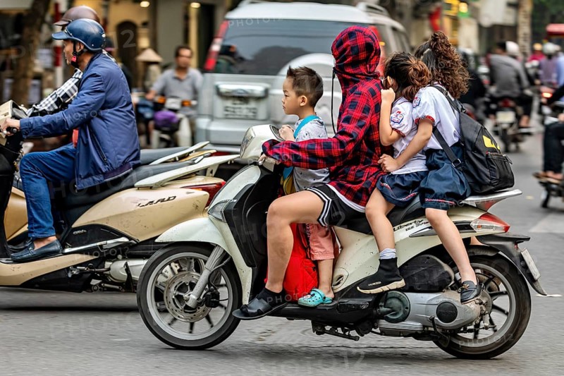 A person with children on a motorbike in a busy city street, woman with children on a scooter in the traffic of Hanoi Vietnam