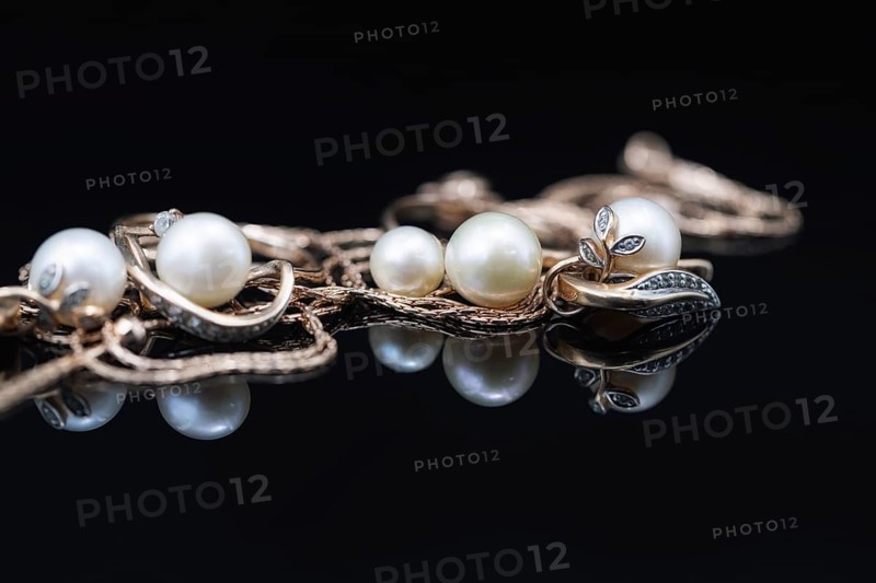 Gold earrings and rings with white pearls lie on a black mirror surface