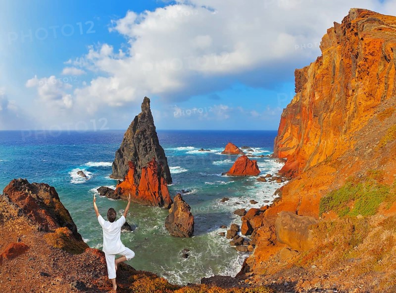 The woman ashore in a white suit for yoga carries out a pose Tree. Atlantic storms. Colorful pinnacles lit sunset. Arid eastern tip of the island of Madeira