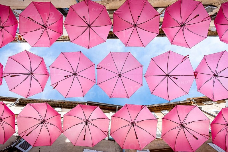 Colorful umbrellas canopy adorning a cozy european alleyway under bright daylight. Grasse, Provence. France