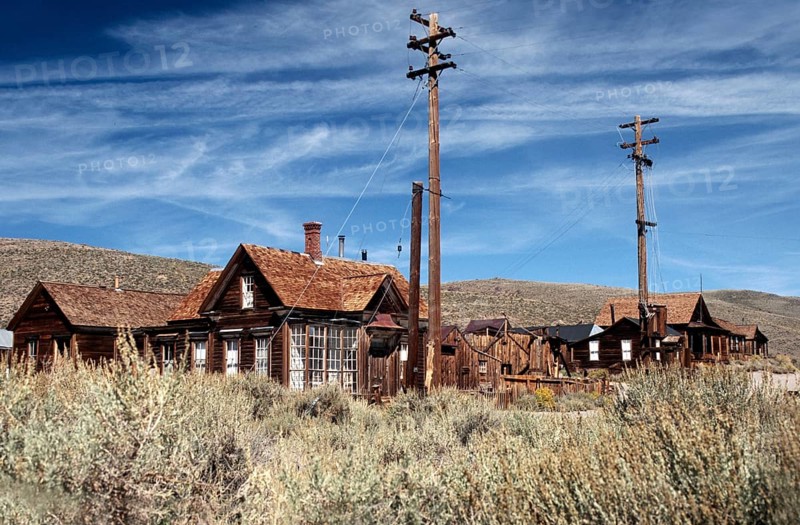 Ghost town of Bodie: Windswept wooden houses, lamp posts and a sweeping view of the surrounding prairie hills. Colour photo, landscape format
