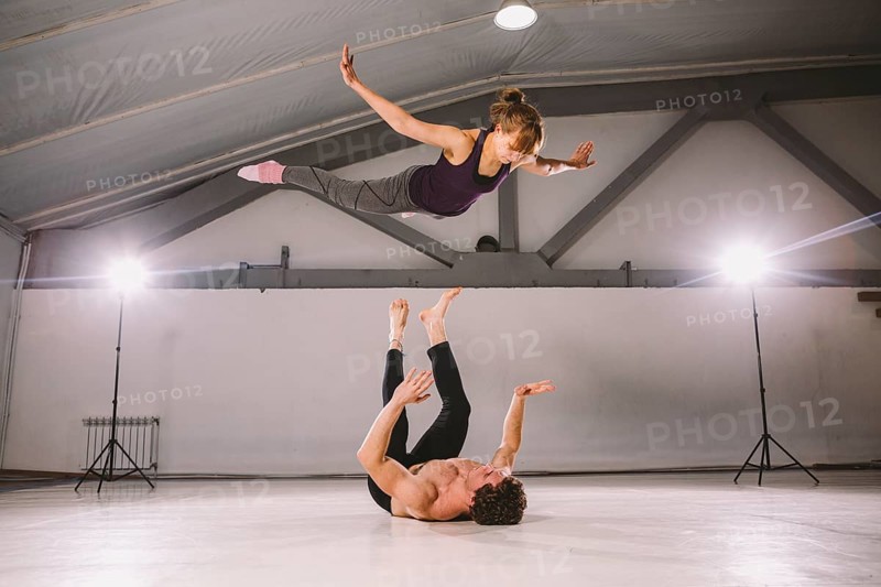 Young couple Couple practicing acro yoga in gym. Healthy lifestyle. Acroyoga. Couple yoga. Partner yoga. Muscular man throwing women to air. Concept of trust, strength and courage