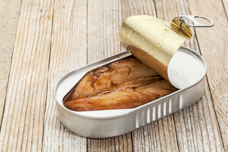 Open can of wild herring in wine sauce against a white painted grunge background