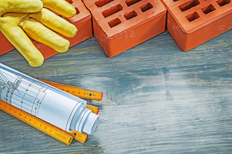 Red bricks leather working gloves construction plans wooden meter on wood board bricklaying concept