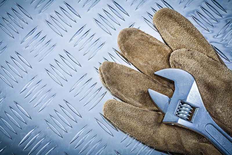 Safety gloves adjustable wrench on grooved metal plate construction concept