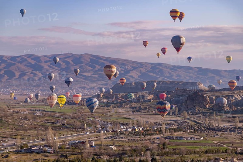 A picture of colorful hot air balloons flying over the landscape of Goreme Historical National Park at sunrise