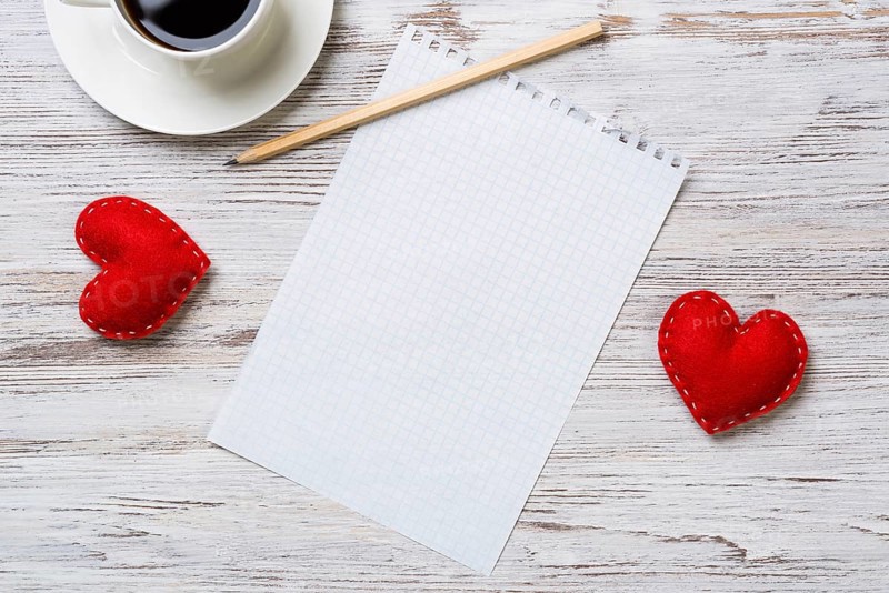 Coffee cup notepad pencil and two red hearts on wooden surface