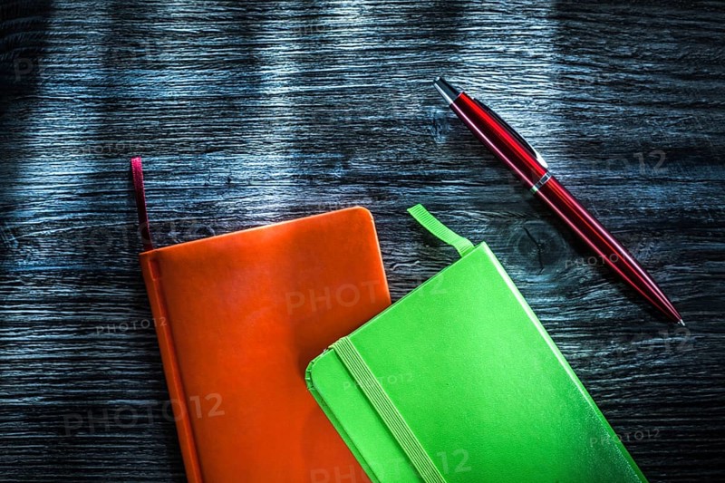 Green and orange notebooks on wooden board