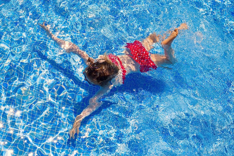 Bikini kid girl swimming on blue tiles pool in summer vacation