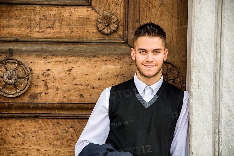 Elegant young man leaning against old wall and wooden door