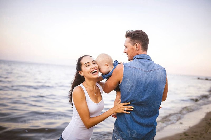Beautiful young family on holiday with baby. The father holds the blonde girl in her arms, and the brunette's mother hugs her husband. The concept of a family beach holiday summer near the sea