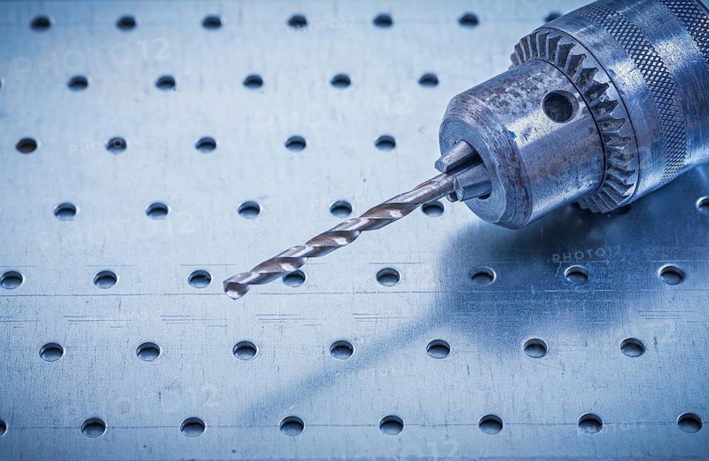 Metal drill on perforated metallic background construction concept