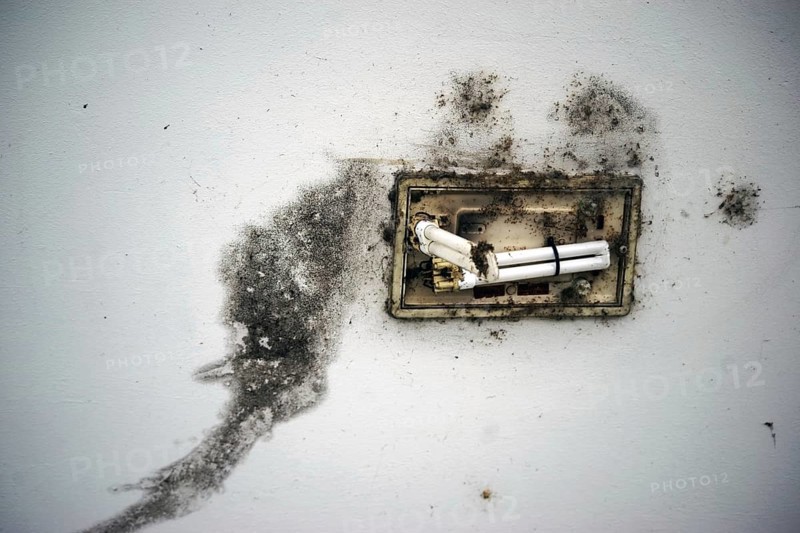 A close-up of a mouldy and dirty ceiling with a broken ceiling light