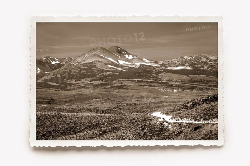 Landscape panorama, the partly snow-covered mountains of the Sierra Nevada rise on the horizon. Photo in sepia tones, white border with jagged edges in the character of old photos, horizontal shadow. Wide landscape panorama, on the horizon the partly snow-capped mountains of the Sierra Nevada rise. Photo in sepia tones, all around a white jagged edge in the character of old photos
