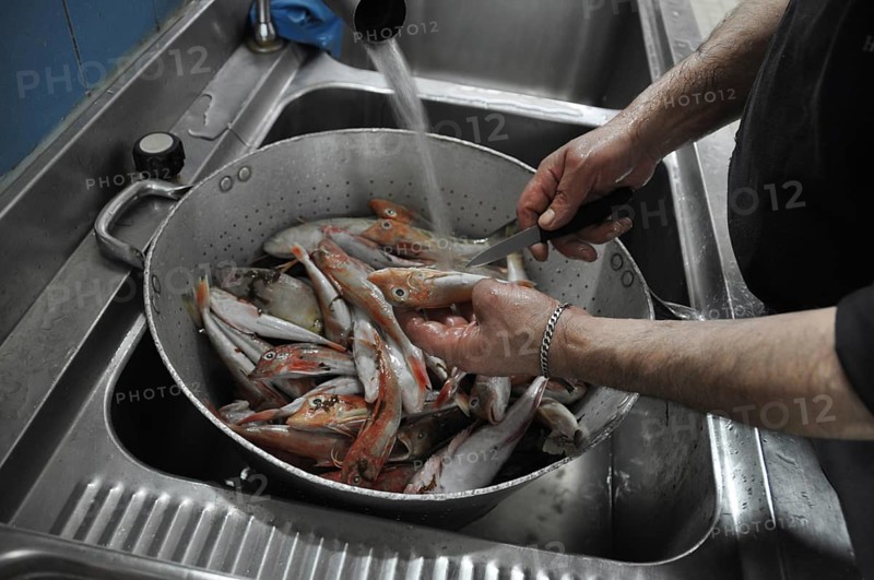 Fish being cleaned and washed in a colander under running water in a kitchen, Cooks and chefs prepare dinner with the typical Mediterranean Diet at a luxury resort in Sciacca, Sicily