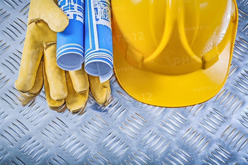 Blue engineering drawings hard hat safety gloves on corrugated metal background construction concept