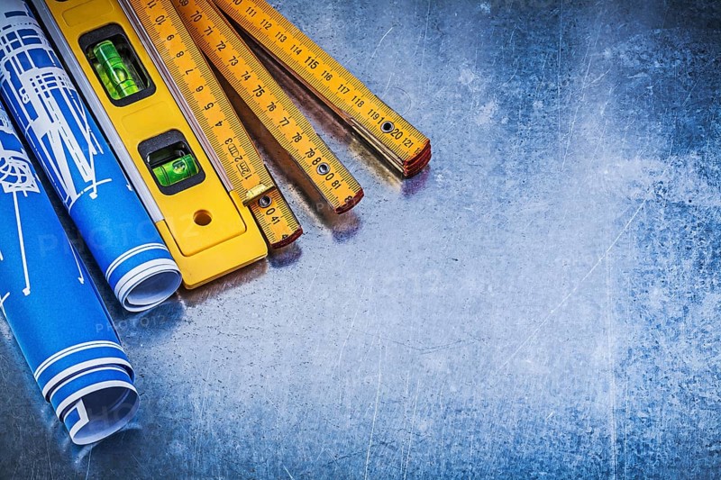 Blue rolled blueprints wooden meter construction level on metallic background