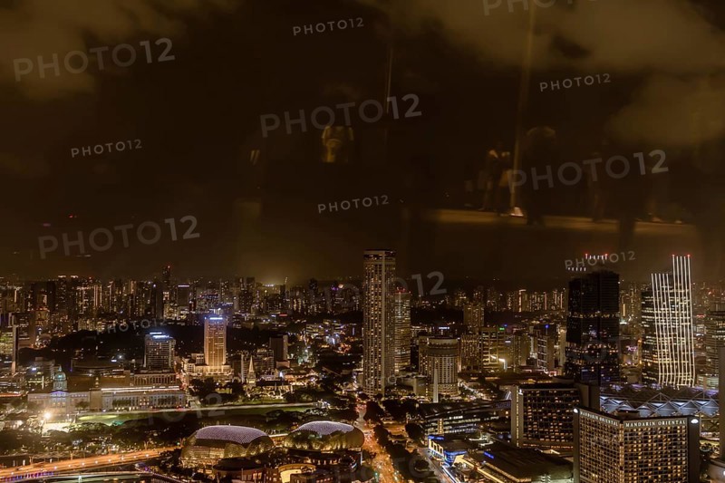 Singapore City, Singapore, January 23, 2019: Beautiful aerial night view of Marina Bay and the surrounding buildings. Reflections cause due to photo taken through window on observation deck, Asia
