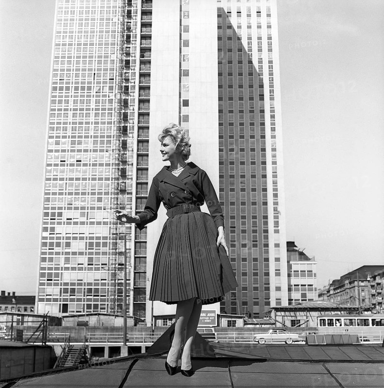 In the 1950s. A woman modelling a 1950s outfit with a jacket and skirt in matching dark. In the background the newly finished skyscraper housing the swedish tax offices. Sweden 1959 Kristoffersson ref CH21
